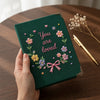 Dark Green Floral Journal Held Beside Golden Pen