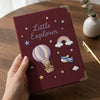 Maroon Little Explorer Notebook Held Beside Gold Pen
