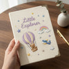 Beige Little Explorer Notebook Held Above Wooden Desk